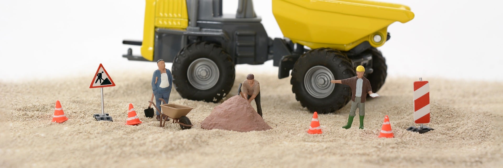 Bouwplaats gemaakt met poppetjes: bouwvakkers met kruiwagen, zandbult, oranje pionnen en verkeersborden voor een shovel.