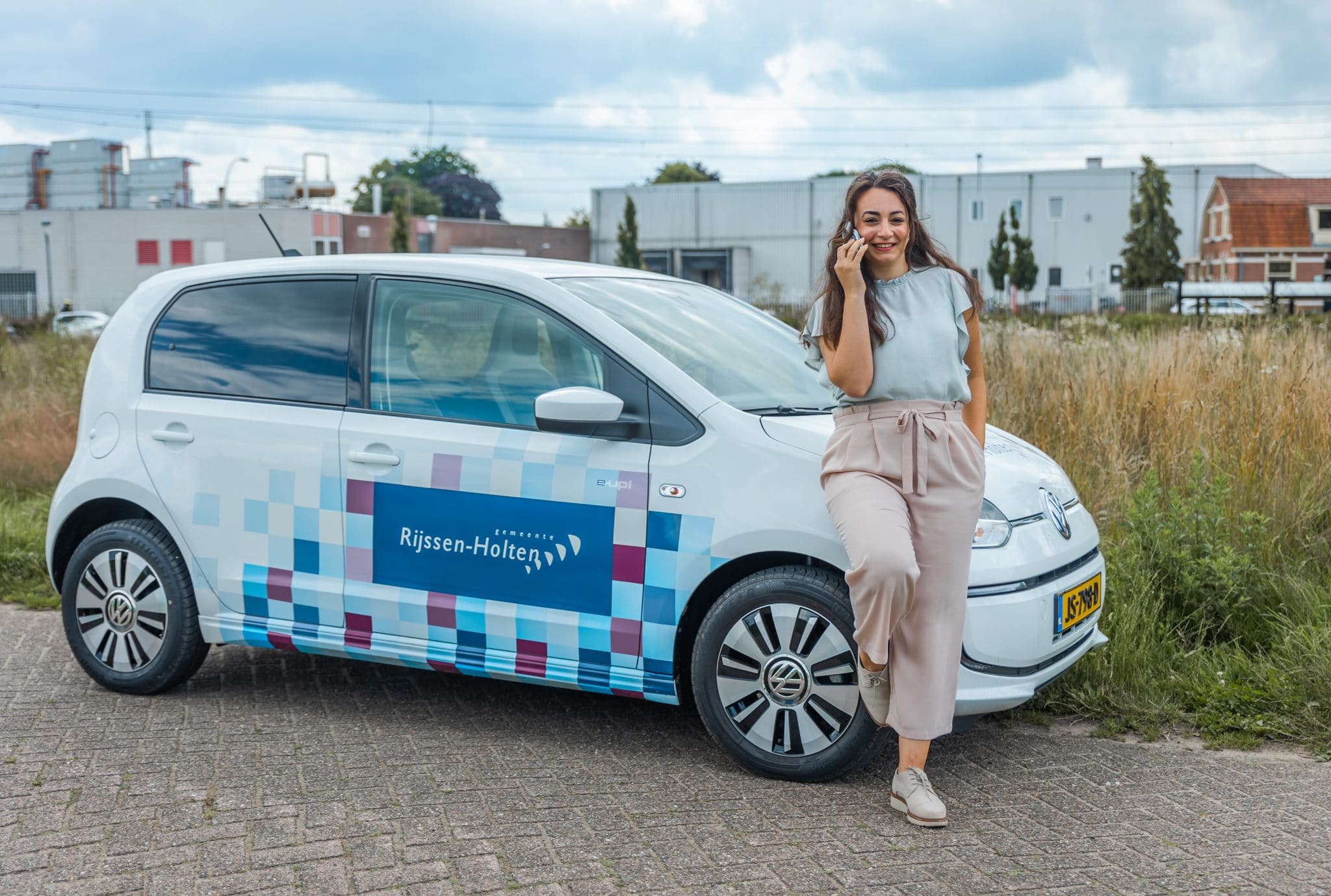 Medewerker Seda Boyukdipi voor de auto van de gemeente, aan het telefoneren