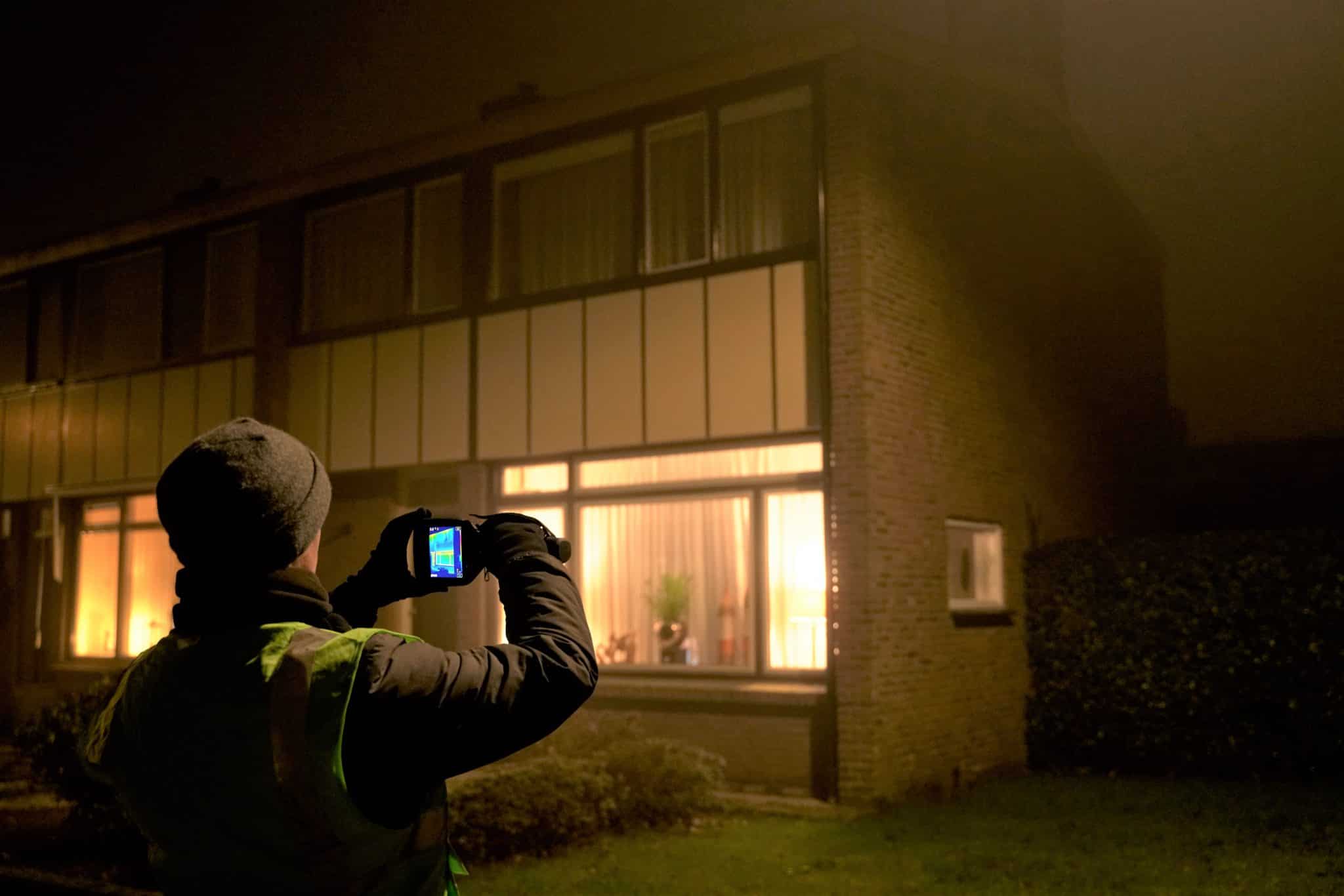 Man maakt een warmtescan van een huis met zijn camera.